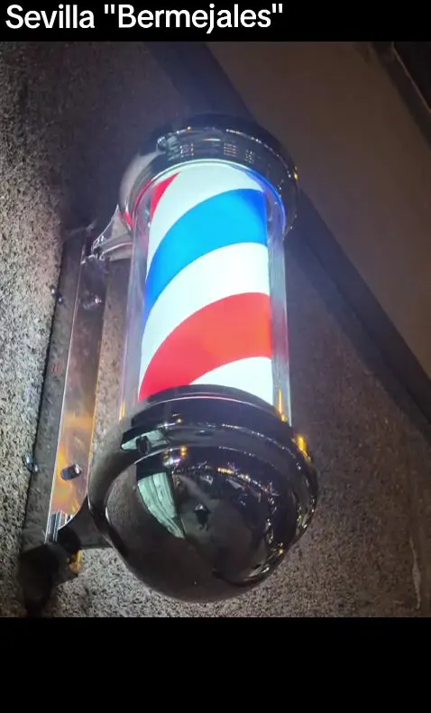 Poste de barbero iluminado en la entrada de la barbería de Bermejales
